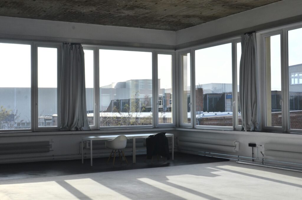 Chairs placed at table near big window with curtain and modern cityscape view with buildings in minimalistic empty room in sunlight